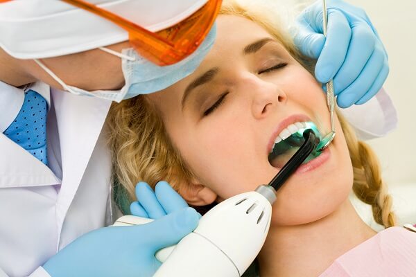 dental patient with uv light being shined in mouth by dentist