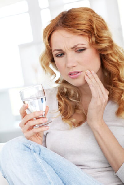 woman holding jaw because her mouth is sensitive, holding glass of water