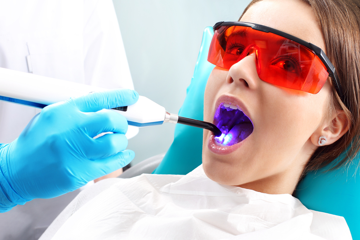 Woman at the dentist's chair during a dental procedure, uv light shined in mouth