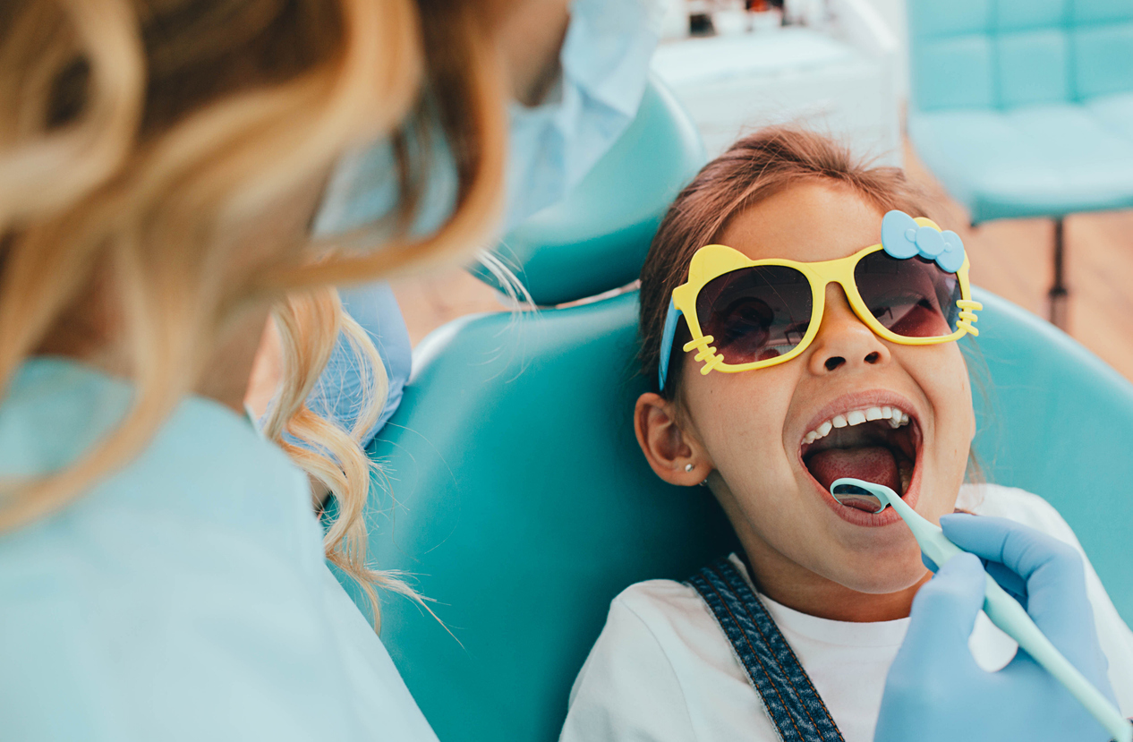 The image shows a little girl at the dentist to explain the importance of regular pediatric dental checkups